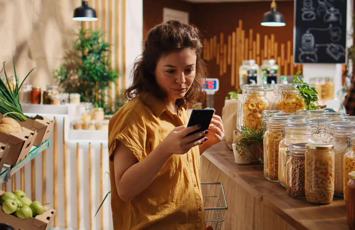 Mujer consultando su móvil en una tienda de productos a granel Mujer consultando su móvil en una tienda de productos a granel